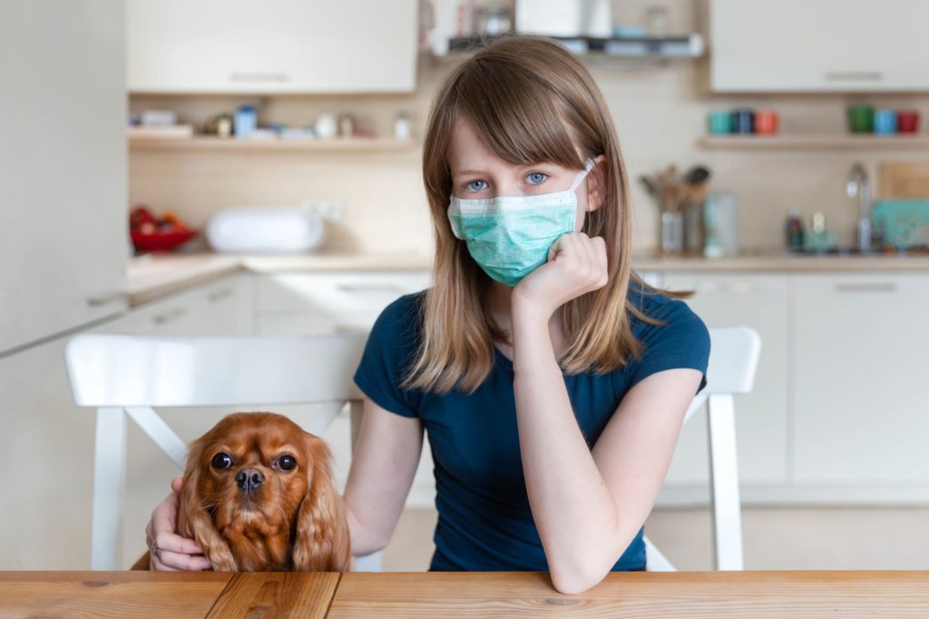 Girl in protective surgical mask with her dog