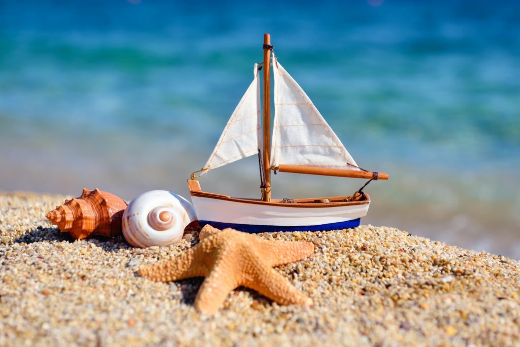 Toy ship and seashells on sand near sea. Summer vacation concept