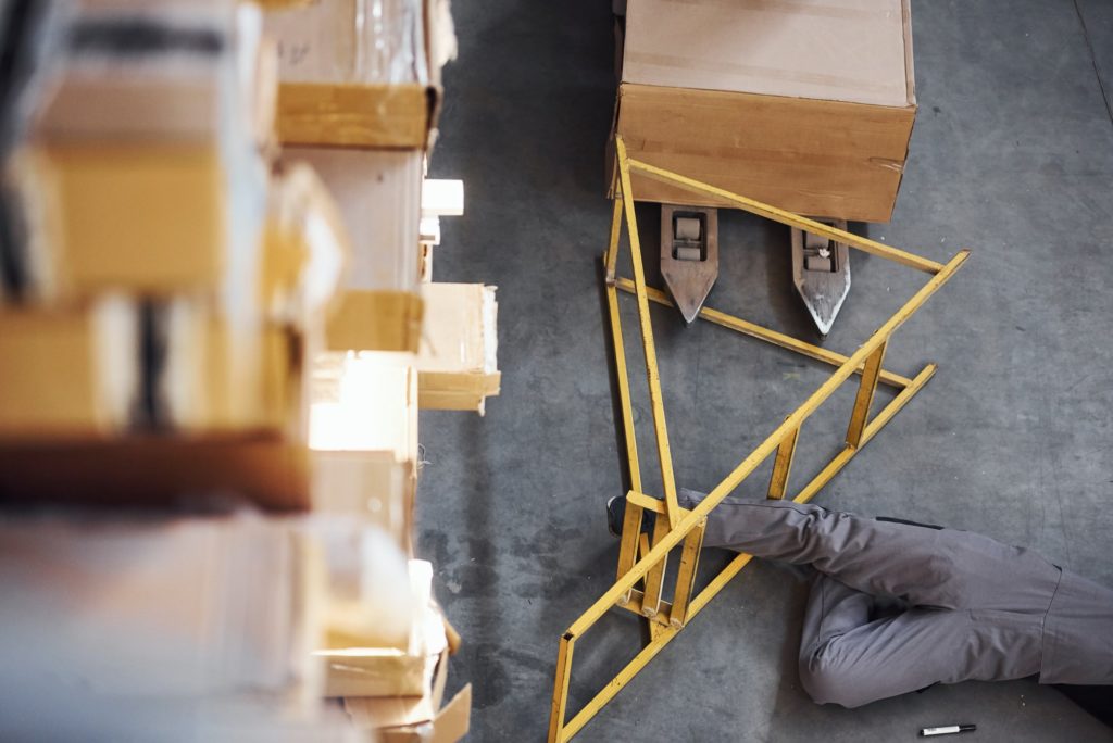 Warehouse worker after an accident in the storage. Man in uniform lying down on the ground